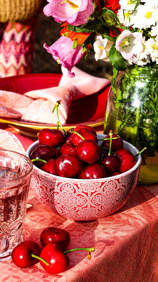 Kirschen in einer rosa Schale neben Blumen und einem Glas