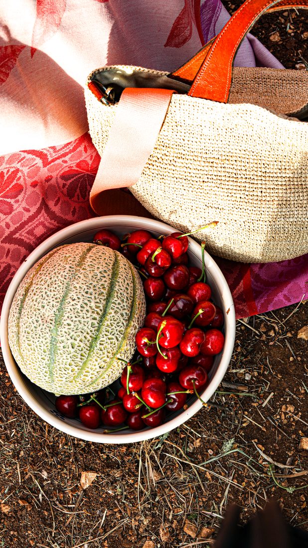 Picknick mit Melone und Kirschen neben einem Bastkorb auf roter Erde