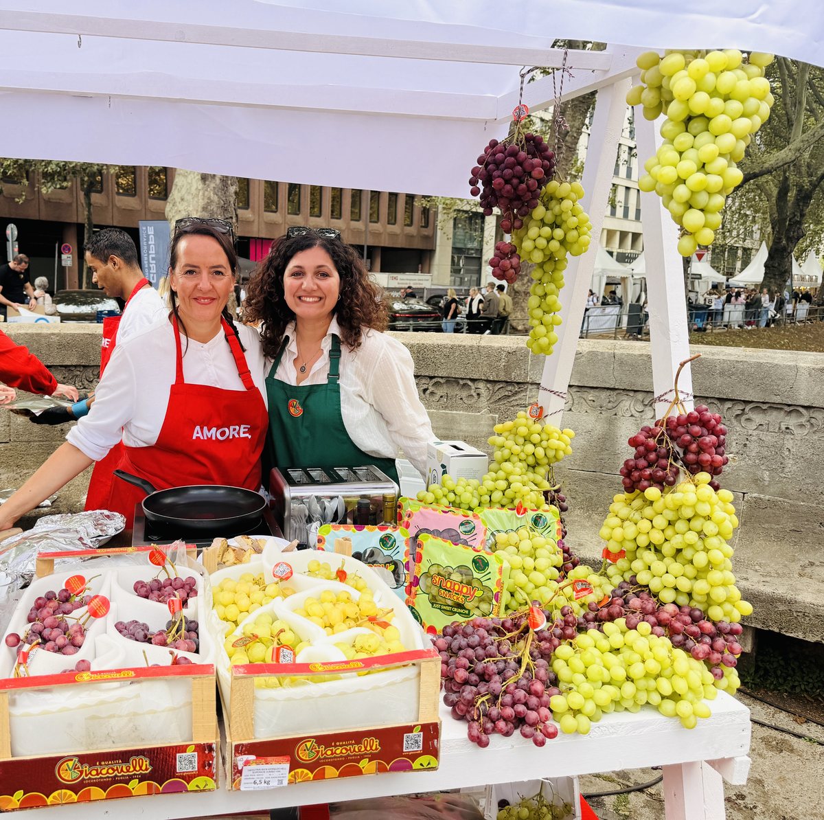 Stefania Lettini in roter AMORE-Schürze und Anna Giacovelli in grüner Giacovelli-Schürze am Traubenstand auf der Königsallee