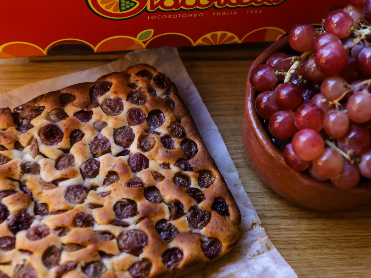 Traubenkuchen mit eingebackenen Trauben und einer Schale roter Trauben vor einer Giacovelli-Kiste