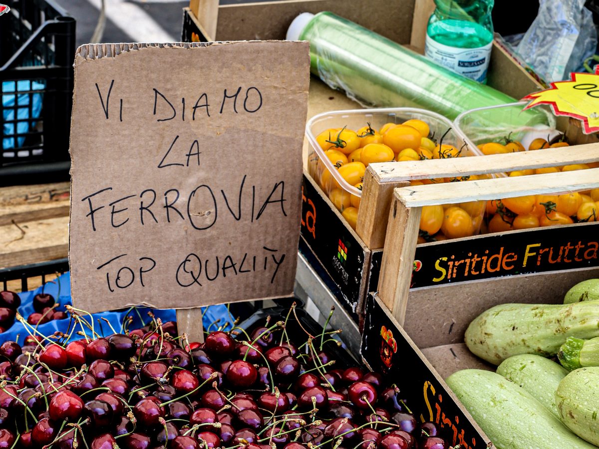 Obst auf einem Markt in Apulien unter einem Pappschild „Vi diamo la ferrovia“