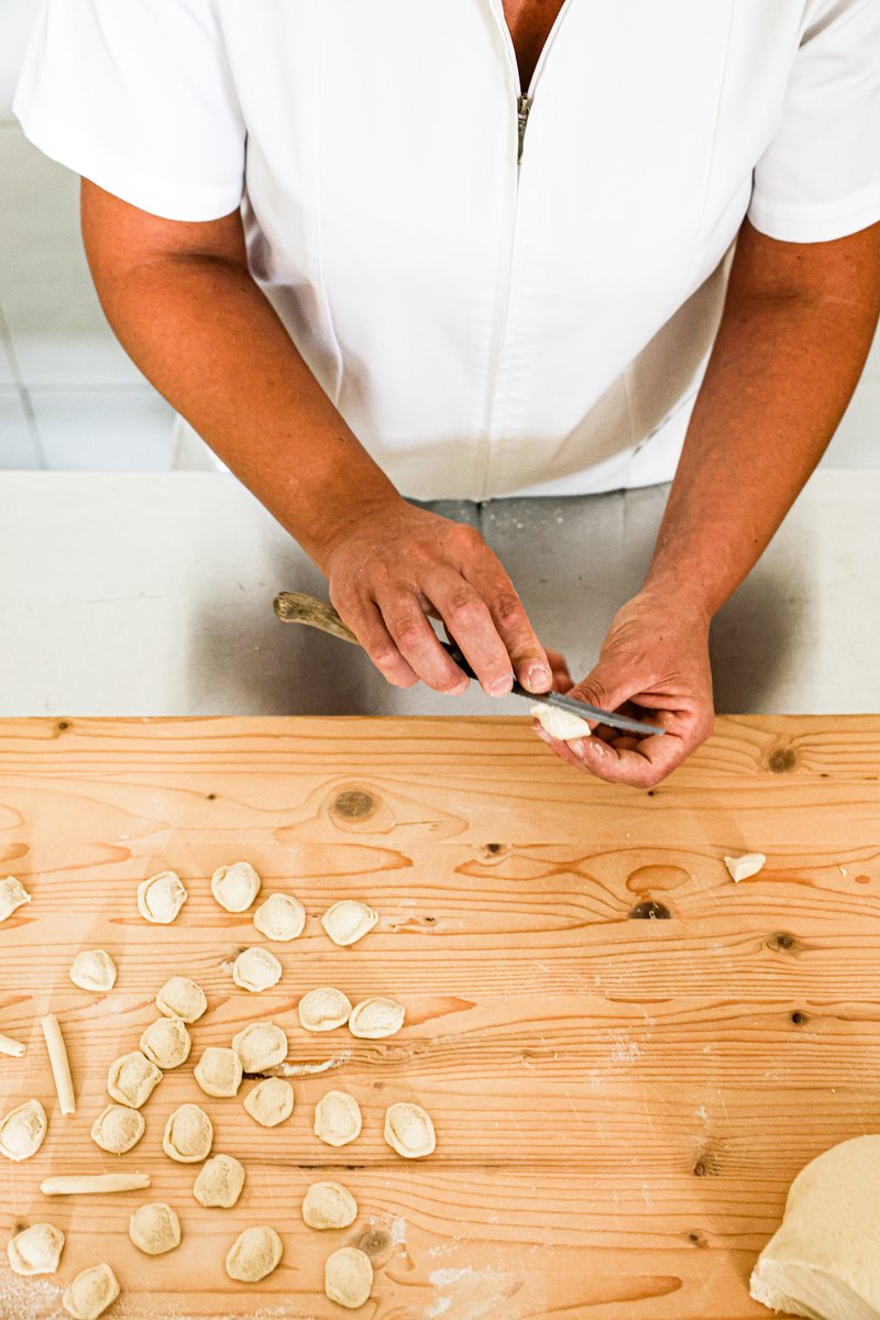 Das Messer gleitet über die Teigstücke, daneben liegen fertige Orecchiette